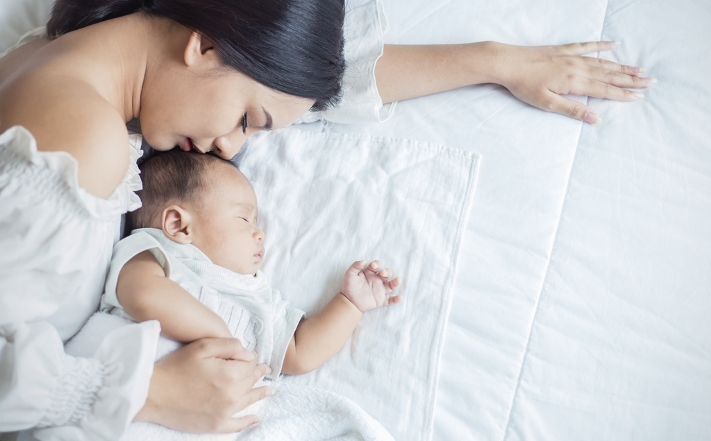 Młoda mama wtulona w noworodka na łóżku