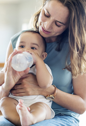 baby drinking milk from bottle on moms lap